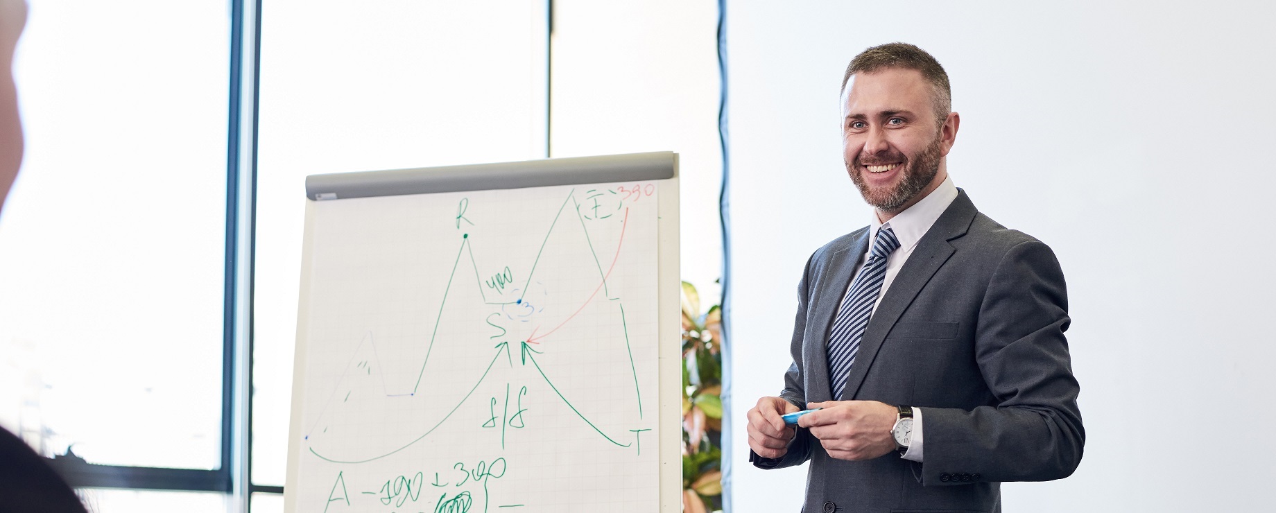 Portrait of bearded business coach smiling cheerfully while standing by whiteboard giving presentation for audience